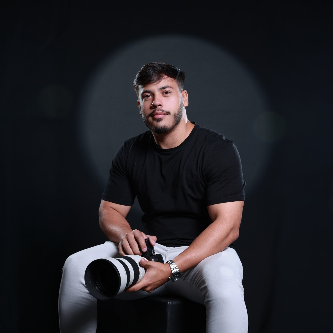 Lucas Praxedes sentado no estúdio com a câmera teleobjetiva no colo